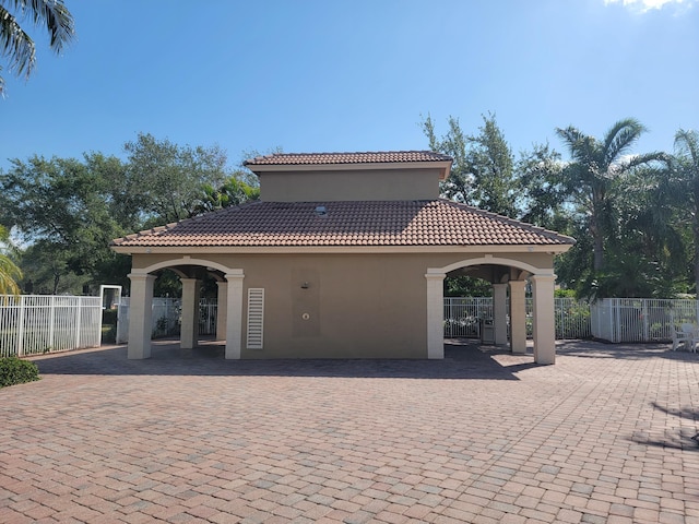 rear view of house with stucco siding, a gate, fence, and a tiled roof