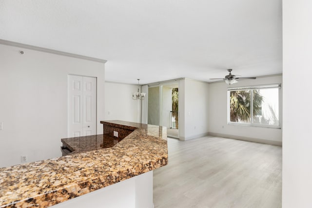 kitchen with light wood finished floors, ceiling fan with notable chandelier, dark stone countertops, baseboards, and ornamental molding