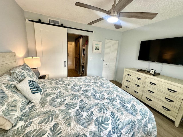 14 Colonial Club Dr Unit 102, Boynton Beach, FL 33435 - bedroom featuring stacked washer / drying machine, a barn door, wood finished floors, a ceiling fan, and a textured ceiling