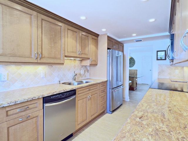 kitchen featuring recessed lighting, a sink, stainless steel appliances, tasteful backsplash, and light stone counters
