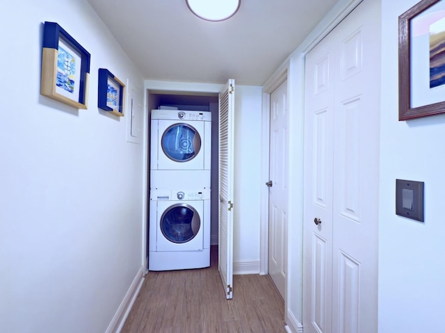 washroom featuring baseboards, stacked washer / dryer, wood finished floors, and laundry area