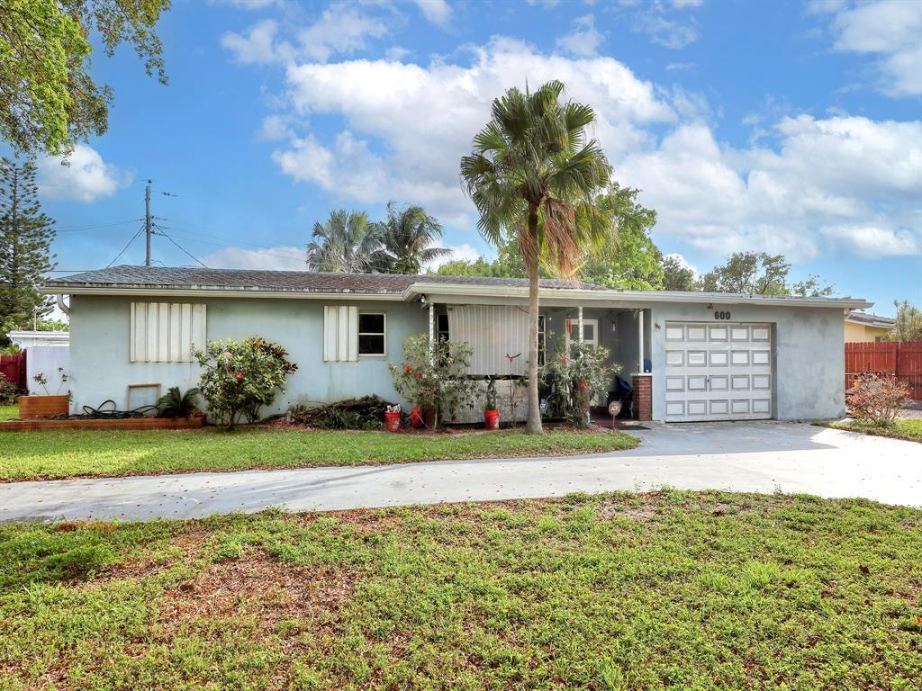 ranch-style home with a front yard, a garage, concrete driveway, fence, and stucco siding