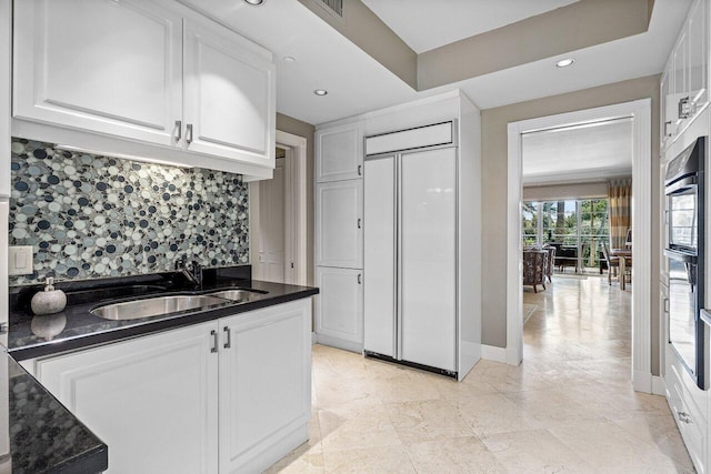kitchen with decorative backsplash, white cabinetry, a sink, oven, and baseboards