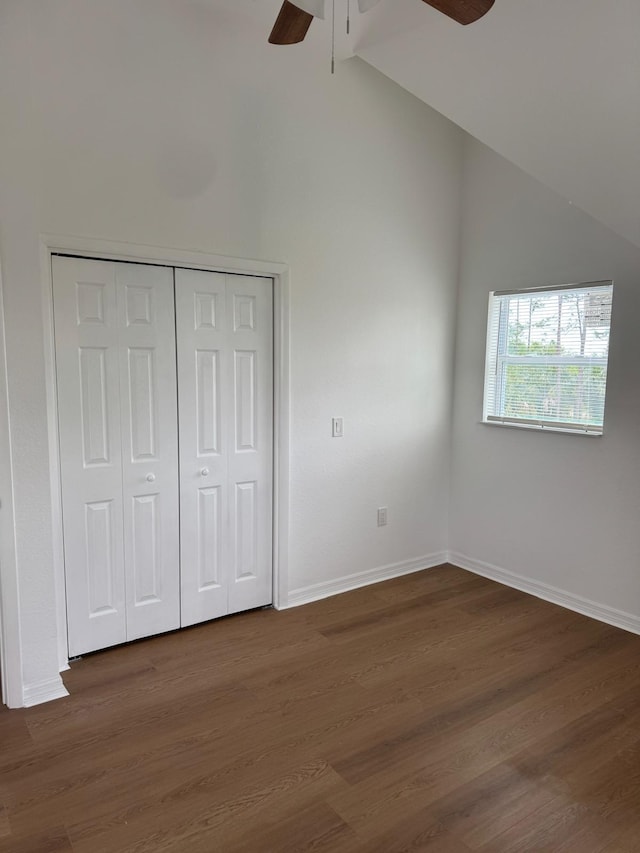 unfurnished bedroom featuring a closet, vaulted ceiling, dark wood-style flooring, a ceiling fan, and baseboards