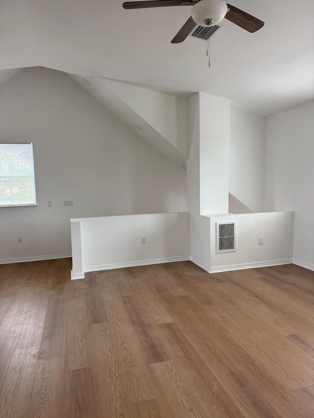 additional living space with wood finished floors, a ceiling fan, visible vents, baseboards, and lofted ceiling
