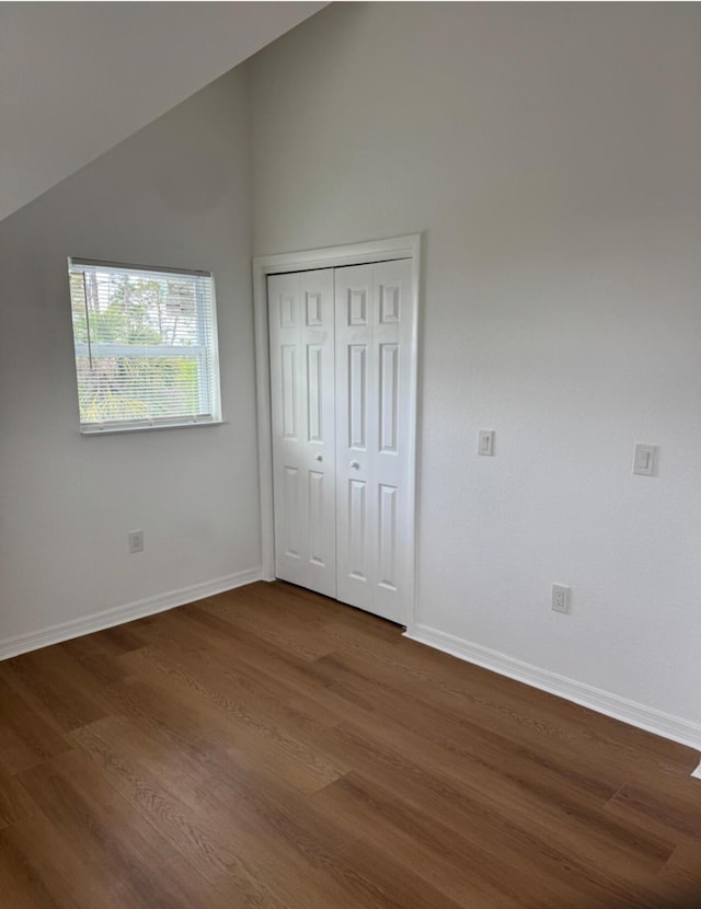 unfurnished bedroom featuring baseboards, a closet, dark wood-style floors, and vaulted ceiling