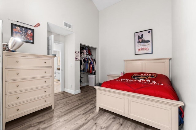 bedroom with visible vents, a closet, baseboards, light wood finished floors, and high vaulted ceiling