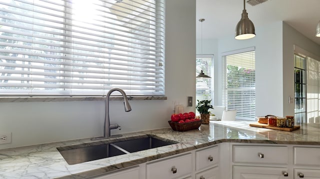 kitchen featuring light stone counters, a sink, white cabinetry, and pendant lighting