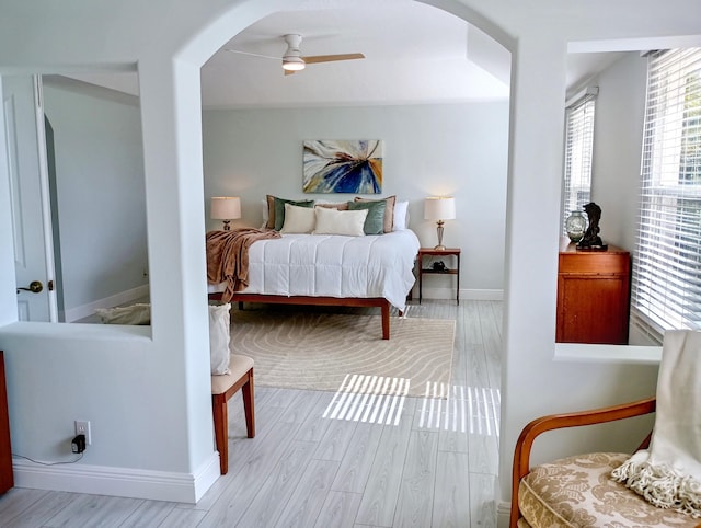bedroom featuring arched walkways, baseboards, a ceiling fan, and wood finished floors