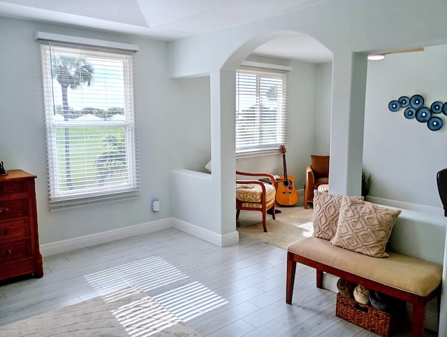 living area with arched walkways, baseboards, plenty of natural light, and light wood-type flooring