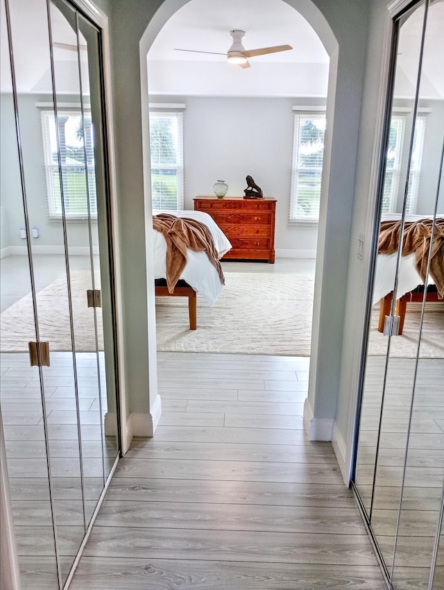 hallway with baseboards, arched walkways, plenty of natural light, and wood finished floors