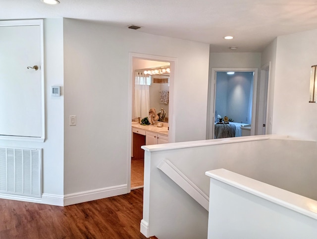 hallway with visible vents, recessed lighting, wood finished floors, and an upstairs landing