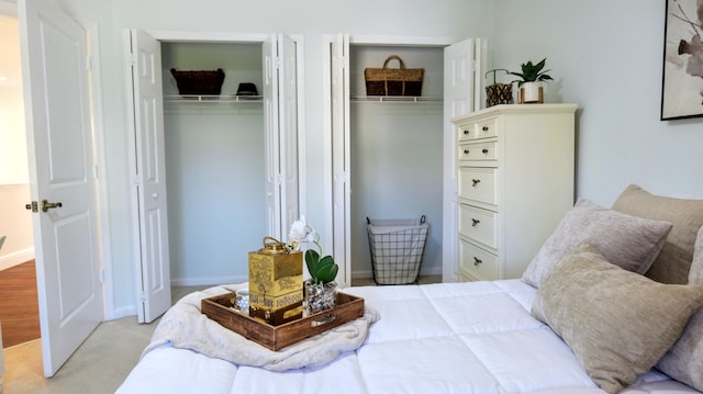 bedroom featuring baseboards, light carpet, and two closets