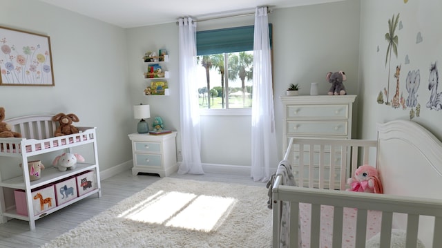 bedroom featuring a nursery area, baseboards, and wood finished floors