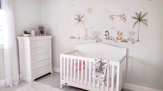 bedroom featuring baseboards, a crib, and wood finished floors