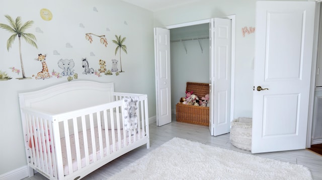 bedroom with a nursery area, baseboards, wood finished floors, and a closet