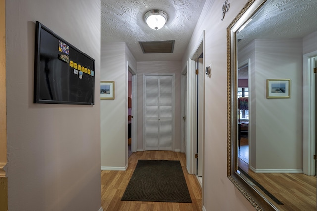 hallway with a textured ceiling, baseboards, and wood finished floors