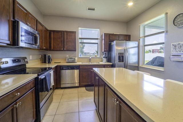kitchen with light countertops, a sink, light tile patterned flooring, dark brown cabinetry, and appliances with stainless steel finishes