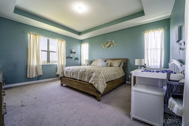 bedroom with carpet floors, a tray ceiling, and baseboards