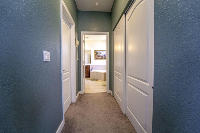 hall featuring a textured wall, carpet flooring, and baseboards