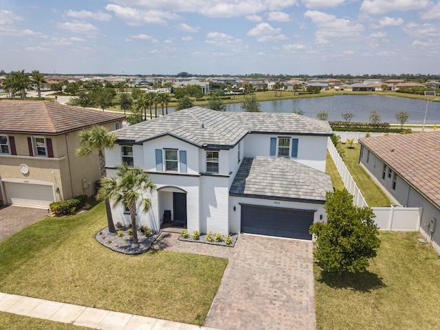 traditional-style home with decorative driveway, a water view, fence, a front yard, and stucco siding