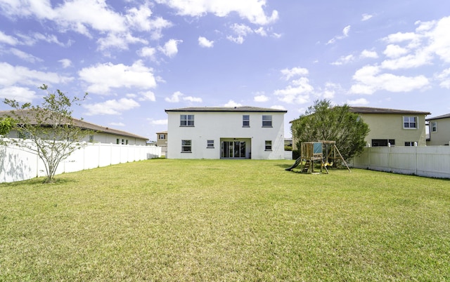 rear view of house featuring a fenced backyard, a yard, a playground, and stucco siding