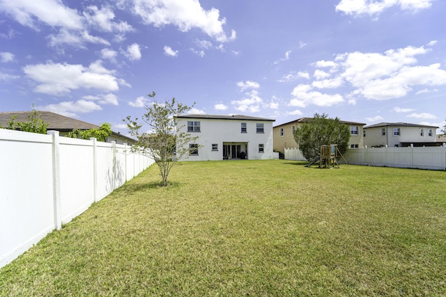 back of house with stucco siding, a lawn, a fenced backyard, and a playground