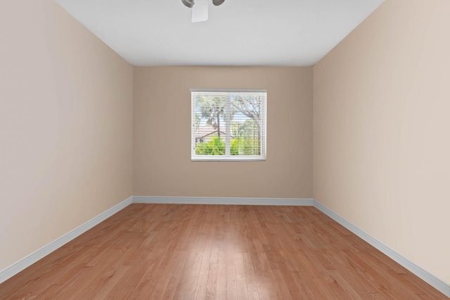 spare room featuring light wood finished floors, a ceiling fan, and baseboards