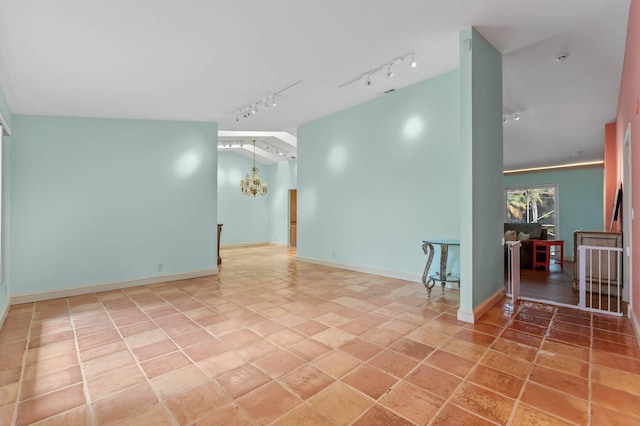 empty room featuring rail lighting, baseboards, and a chandelier