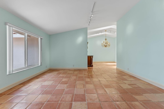 spare room with vaulted ceiling, rail lighting, baseboards, and a notable chandelier