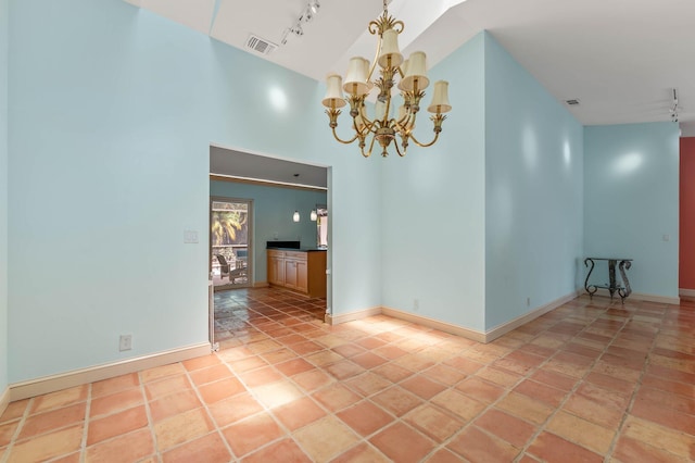 empty room featuring track lighting, a chandelier, a towering ceiling, and visible vents