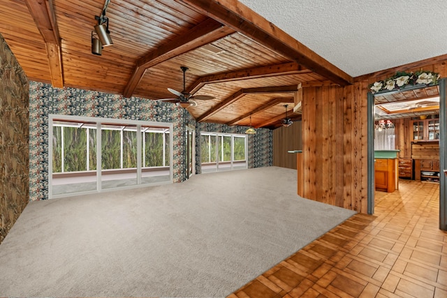 unfurnished living room featuring wood walls, beam ceiling, ceiling fan, and wallpapered walls