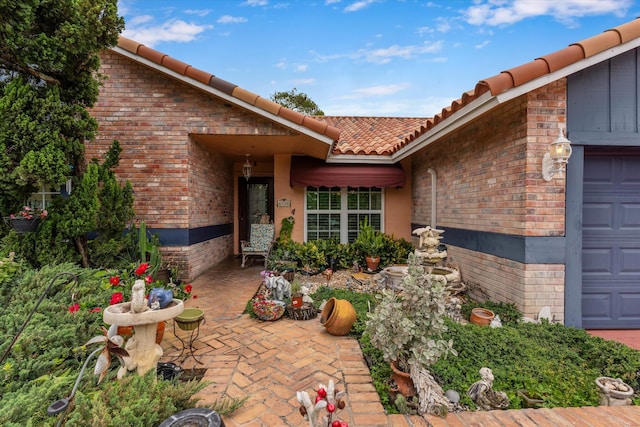 doorway to property with an attached garage, a tiled roof, brick siding, and stucco siding