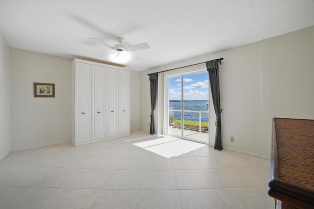 unfurnished bedroom with a water view, access to exterior, ceiling fan, baseboards, and light tile patterned flooring