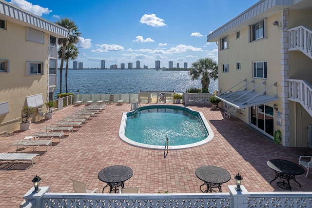 community pool with fence, a water view, and a patio area