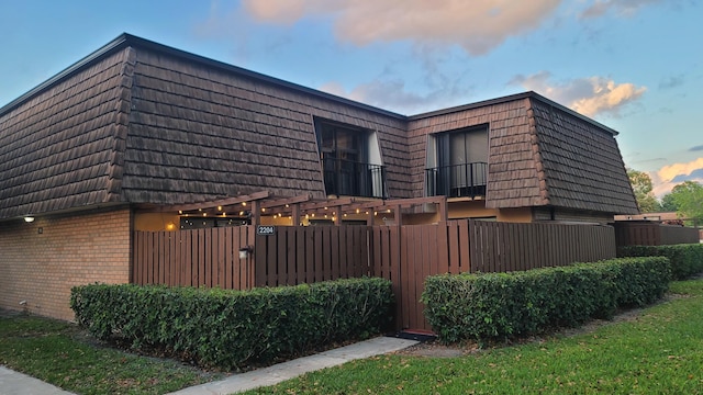 view of side of home with brick siding, a balcony, a tiled roof, and mansard roof