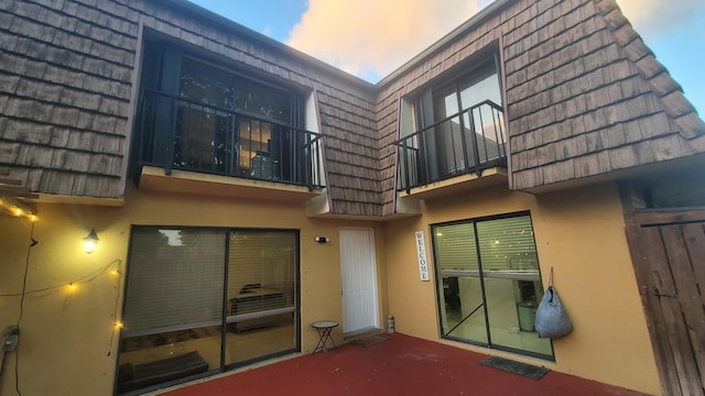 back of house with a patio, mansard roof, and stucco siding