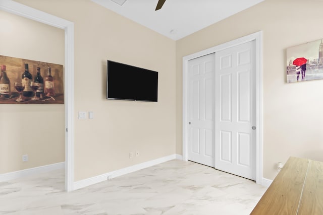 unfurnished bedroom with light marble finish floors, a closet, baseboards, and ceiling fan
