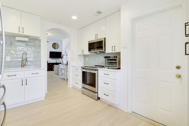 144 Pennock Landing Cir, Jupiter, FL 33458 - kitchen with stainless steel appliances, tasteful backsplash, arched walkways, light wood-type flooring, and white cabinetry