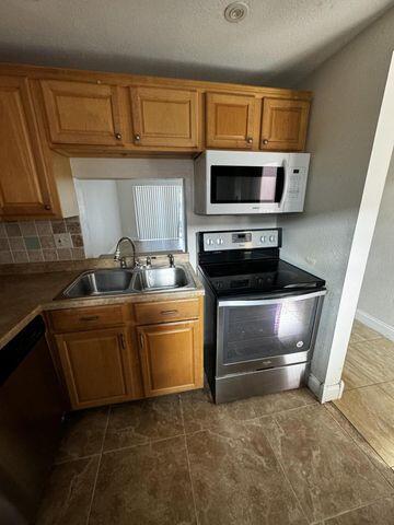 kitchen with brown cabinetry, tasteful backsplash, a sink, stainless steel appliances, and baseboards