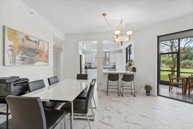 dining area with a textured ceiling, a healthy amount of sunlight, marble finish floor, and a notable chandelier