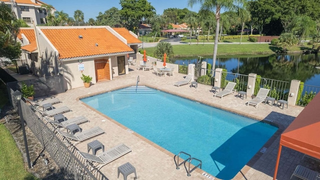 community pool with a water view, fence, central AC unit, and a patio