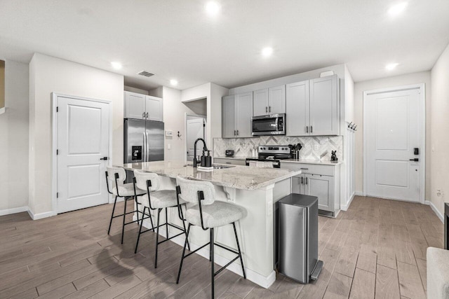 5612 Mentmore Dr, West Palm Beach, FL 33407 - kitchen featuring stainless steel appliances, a sink, light wood-style floors, a breakfast bar area, and baseboards