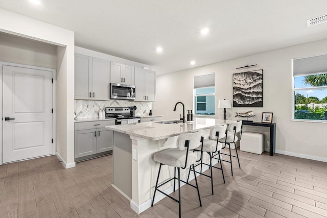 5612 Mentmore Dr, West Palm Beach, FL 33407 - kitchen with stainless steel appliances, a sink, tasteful backsplash, a center island with sink, and light wood-style flooring