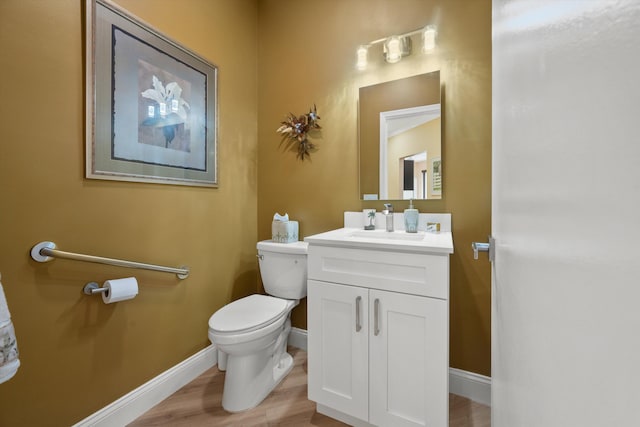half bathroom with toilet, wood finished floors, vanity, and baseboards