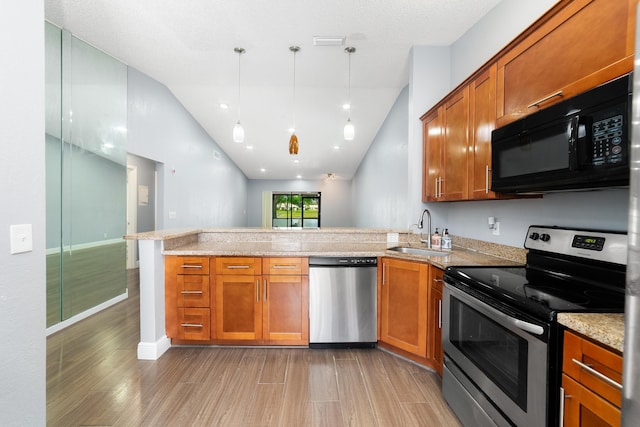 kitchen featuring light wood-style flooring, a peninsula, appliances with stainless steel finishes, a sink, and brown cabinets