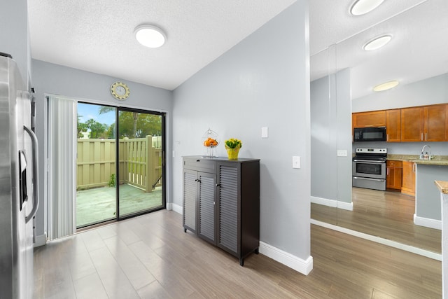 kitchen featuring brown cabinets, light wood-type flooring, appliances with stainless steel finishes, and vaulted ceiling
