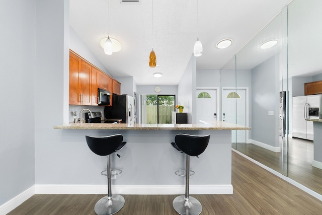 kitchen featuring dark wood-type flooring, brown cabinets, appliances with stainless steel finishes, and a kitchen breakfast bar