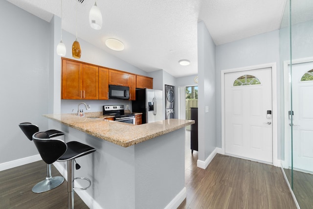 kitchen featuring dark wood finished floors, a kitchen bar, brown cabinetry, stacked washer / dryer, and appliances with stainless steel finishes