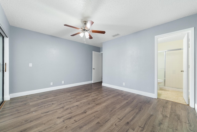 unfurnished bedroom with baseboards, ensuite bathroom, a textured ceiling, visible vents, and wood finished floors